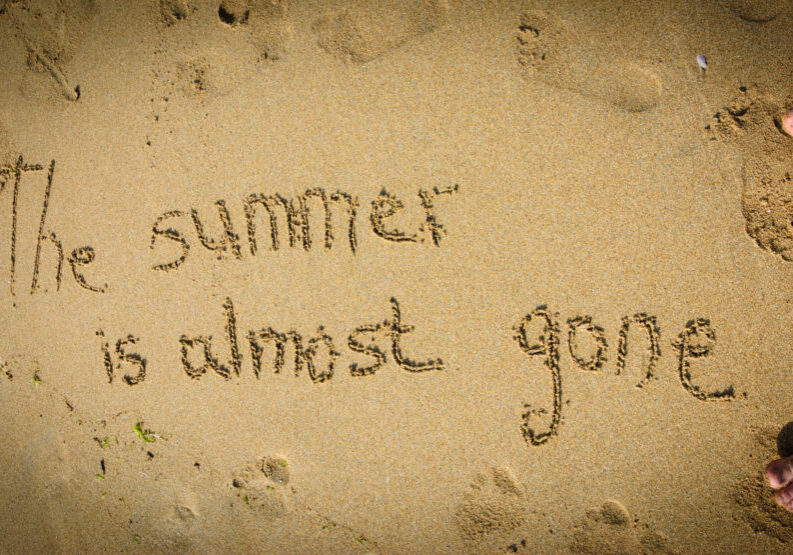 A sentence written on the sand of a beach: THE SUMMER IS ALMOST GONE, footprints and female foots . Vacation end / back from holiday / back to the work or school concept. Vignette effect.